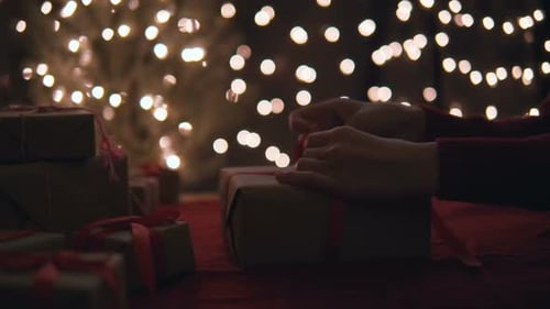 Hands Tying Gift Ribbon Under Holiday Lights