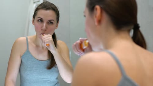 Woman Brushing Teeth in Front of Mirror