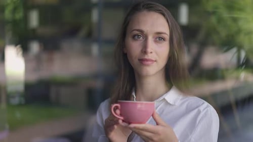 Brunette Caucasian Woman with Brown Eyes Looking Out Window Drinking Coffee in Slow Motion in Cafe