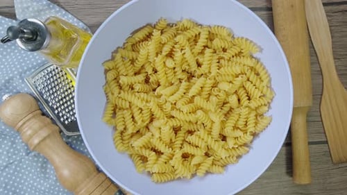 Fusilli Pasta Dry on the Table Slowly Rotates. Blue Plate on Wooden Background. Top View.