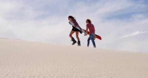 Couple walking with sand boards in the desert