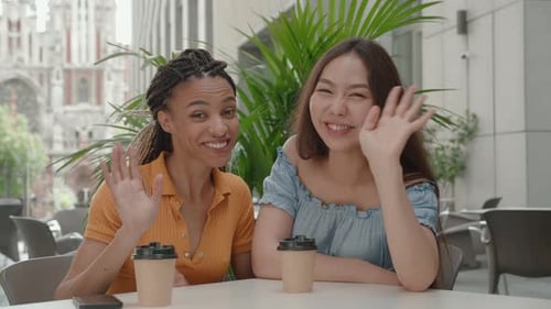 Two Smiling Happy Girlfriends Woman Vlogger Speaking Looking at Camera Sitting in Cafe