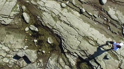 Side view tracking shot of a young man running on a rocky ocean beach shoreline.
