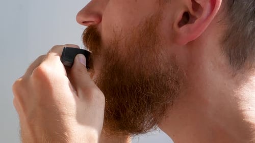 Adult man cutting his own beard and mustache with scissors comb Caucasian red bearded male face 4K