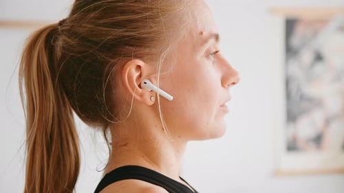 Woman Adjusts Earbud During Home Workout