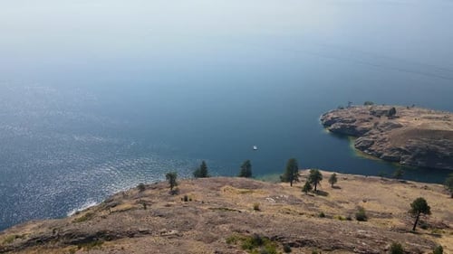 Small boat anchored near the dry and rocky shore of Okanagan Lake during wildfire season. Aerial des