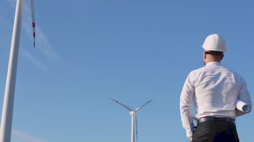 The Engineer Stands with His Back to the Camera on the Background of Windmills and Rejoices with His