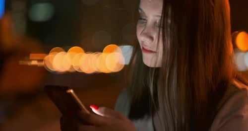 Young Girl in the Night City Writes Text Messages in a Smartphone