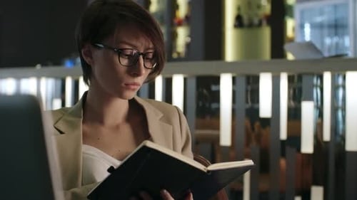 Woman Reads Notebook at Urban Cafe