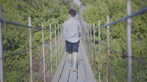 Guy Walks on Suspended Bridge in the Forest