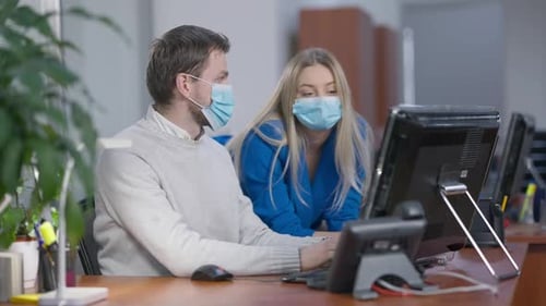 Confident Caucasian Man and Woman in Coronavirus Face Masks Talking Messaging Online in Office