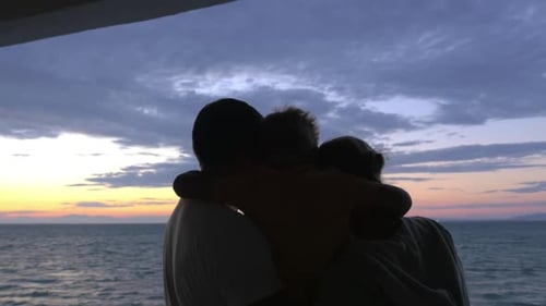 El hijo abraza a madre y padre contra el atardecer en el mar