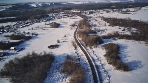 Luftaufnahme einer Asphaltstraße, umgeben von Schnee auf dem Land