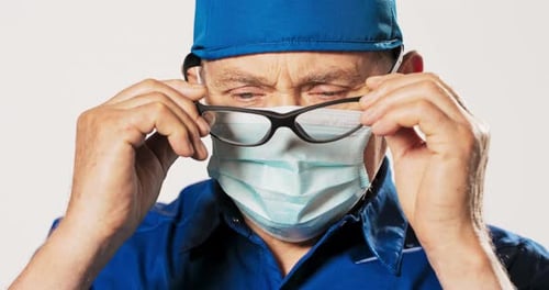 Doctor puts on glasses wearing surgical cap and mask