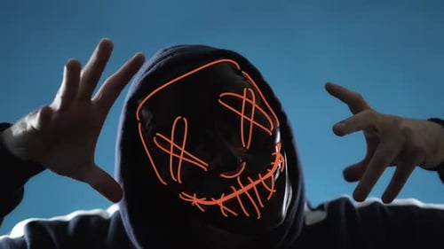 Hooded Figure in Glowing Mask Raises Hands