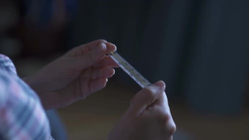 As mãos das mulheres seguram um termômetro de mercúrio para verificar a temperatura