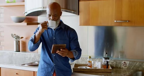 Senior Man Using Digital Tablet While Having Black Coffee in Kitchen