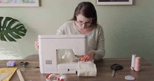 Adult Woman Sews on a Sewing Machine Sitting at Home at Table