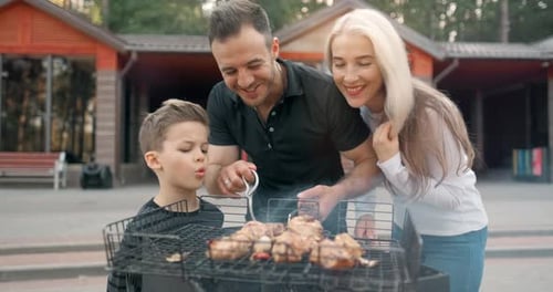 Happy Family Cook Meat on Grill. Father and Mother with Son Fry Sausages on Grill and Smiling. Slow