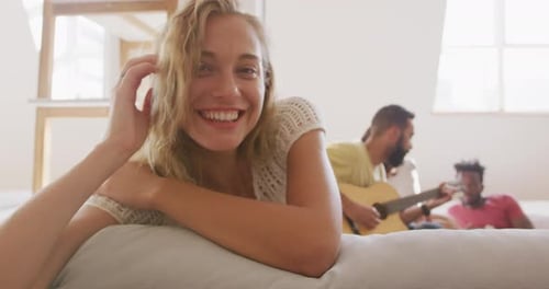 Woman Smiling on Couch with Friends Playing Guitar