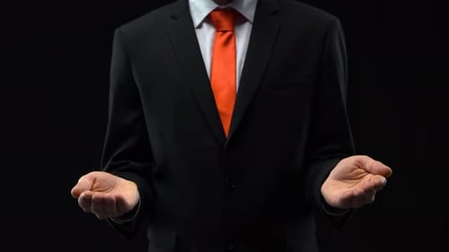 Male in Black Suit Opens Palms at Black Background. Mockup Ready for Your Text or Product.