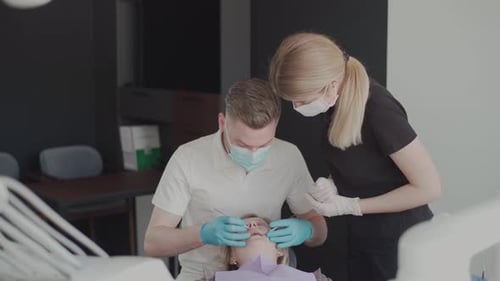 Dentist Examining Patient Teeth with Assistant