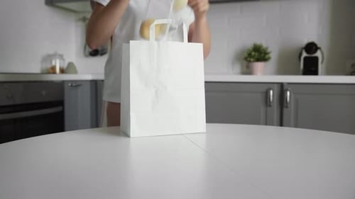 Mujer joven desempacando bolsa de compras con verduras en la cocina en mesa de madera. Hogar Cero Desechos