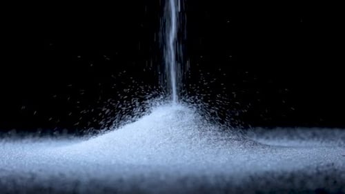 Partikel aus weißem, trockenem Sand strömen herab und bilden einen Hügel auf einem isolierten schwarzen Hintergrund mit