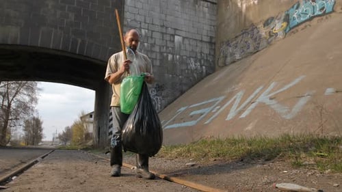 Man picking up litter with stick on gravel road
