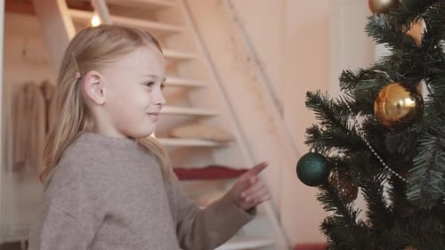 Smiling Girl Touches Christmas Tree Ornament