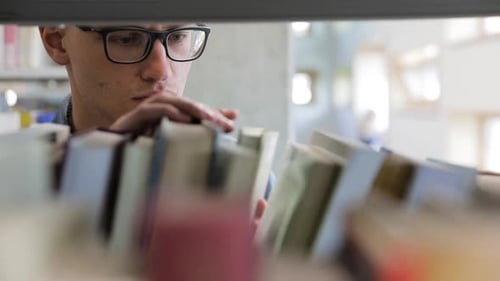 Man Looking For Book On Bookshelves At Library At College