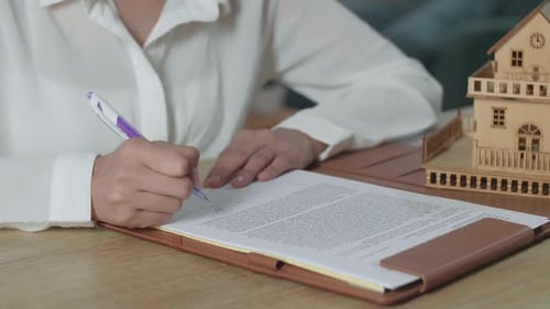 Close Up Of A Woman Holding A Pen And Signing On House Purchase Contract Paper