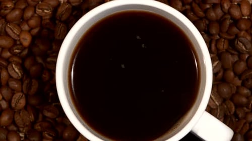 White Cup with Coffee Stands on Brown Beans, Sacking, Close Up, Rotation