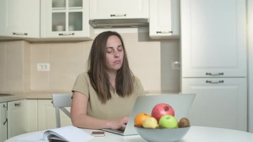 Woman Using Laptop in Kitchen Stretches Neck