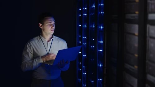 Man Working in Dark Server Room with Laptop