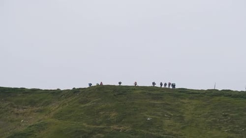 Group of Tourists with Hiking Backpacks Climbs the Mountain Range. Afar View