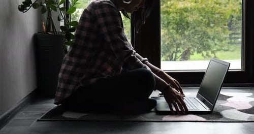 Freelancer Woman Typing on Laptop Sitting on the Floor at Home Near Large Windows