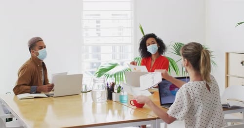 Woman wearing face mask showing a document to her colleague at office