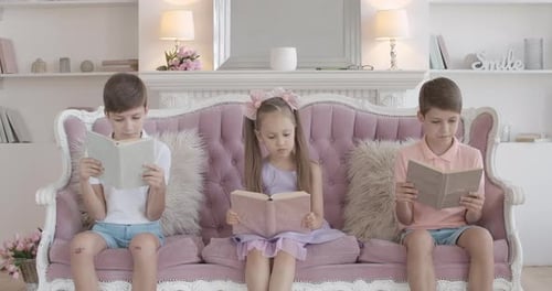 Three Children Reading Books on Pink Couch