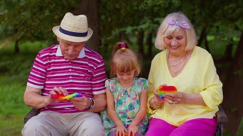 Un couple senior élégant, grand-mère, grand-père et petite-fille, jouent au jeu de jouets antistress Pop It