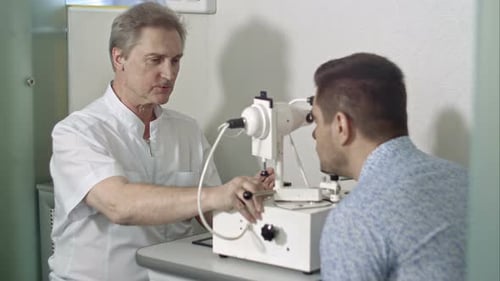 Elderly Female Ophthalmologist and Male Client Checking Eyesight in Clinic