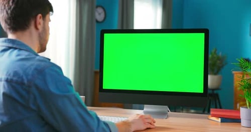 Man benutzt All-in-One-Computer mit grünem Mockup-Bildschirm, während er am Schreibtisch sitzt