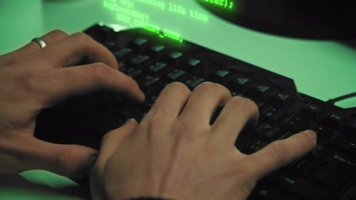 Gros plan sur les mains d'un hacker tandis que des caractères de code vert sortent du clavier dans le Dark Office