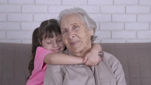 Child Hugging Grandmother on Couch Indoors