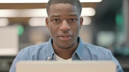 Happy Young Adult Smiles at Laptop