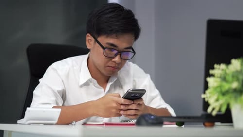 Young Man Using Smartphone at Desk in Office