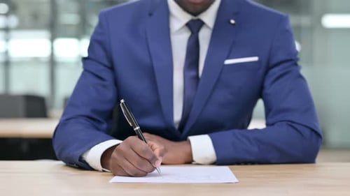 Close Up of African Businessman Writing on Paper