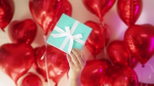 Hand Holds Gift Box with Red Heart Balloons