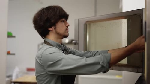 Cuisinier masculin ouvrant le four et mettant une tarte crue dans la cuisine