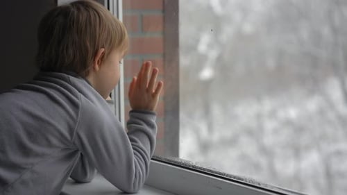 A Little Boy Looks Through the Window on a Heavy Snowfall Waiting for Christmas To Come